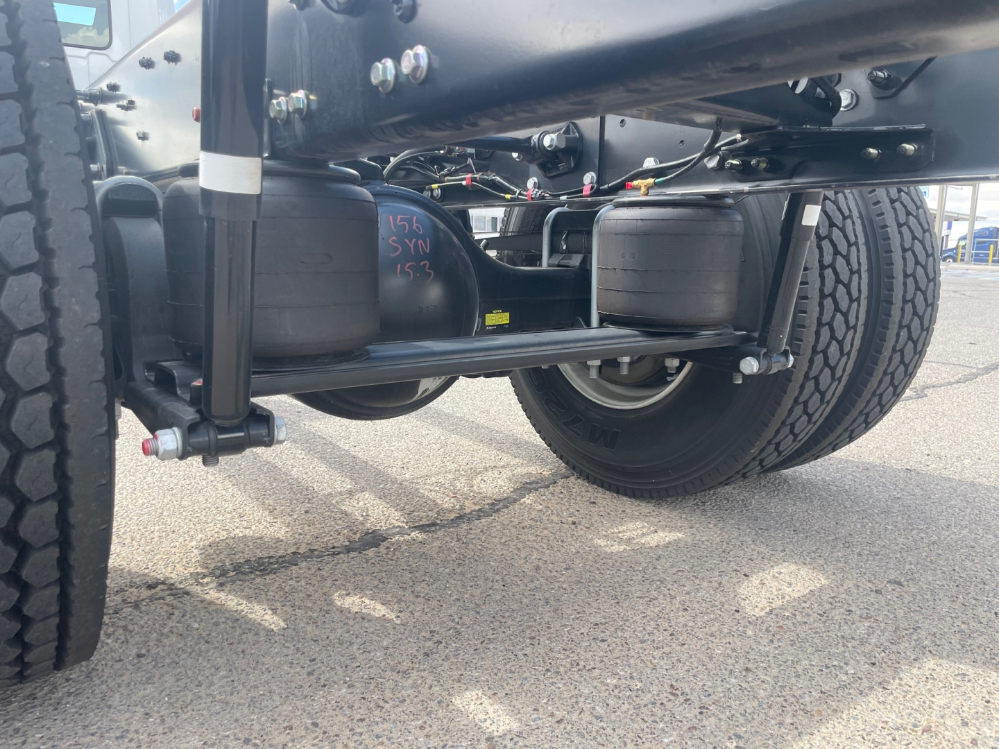 Hino L6 cab and chassis undercarriage showing rear axle and dual-tire setup with fuel tank, hoses, and frame. visible text on badge: 157 SX 153 (on black component).