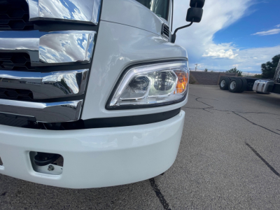 Front left corner of a 2025 Hino L6 cab and chassis showing headlight and chrome grille with blue sky reflection.