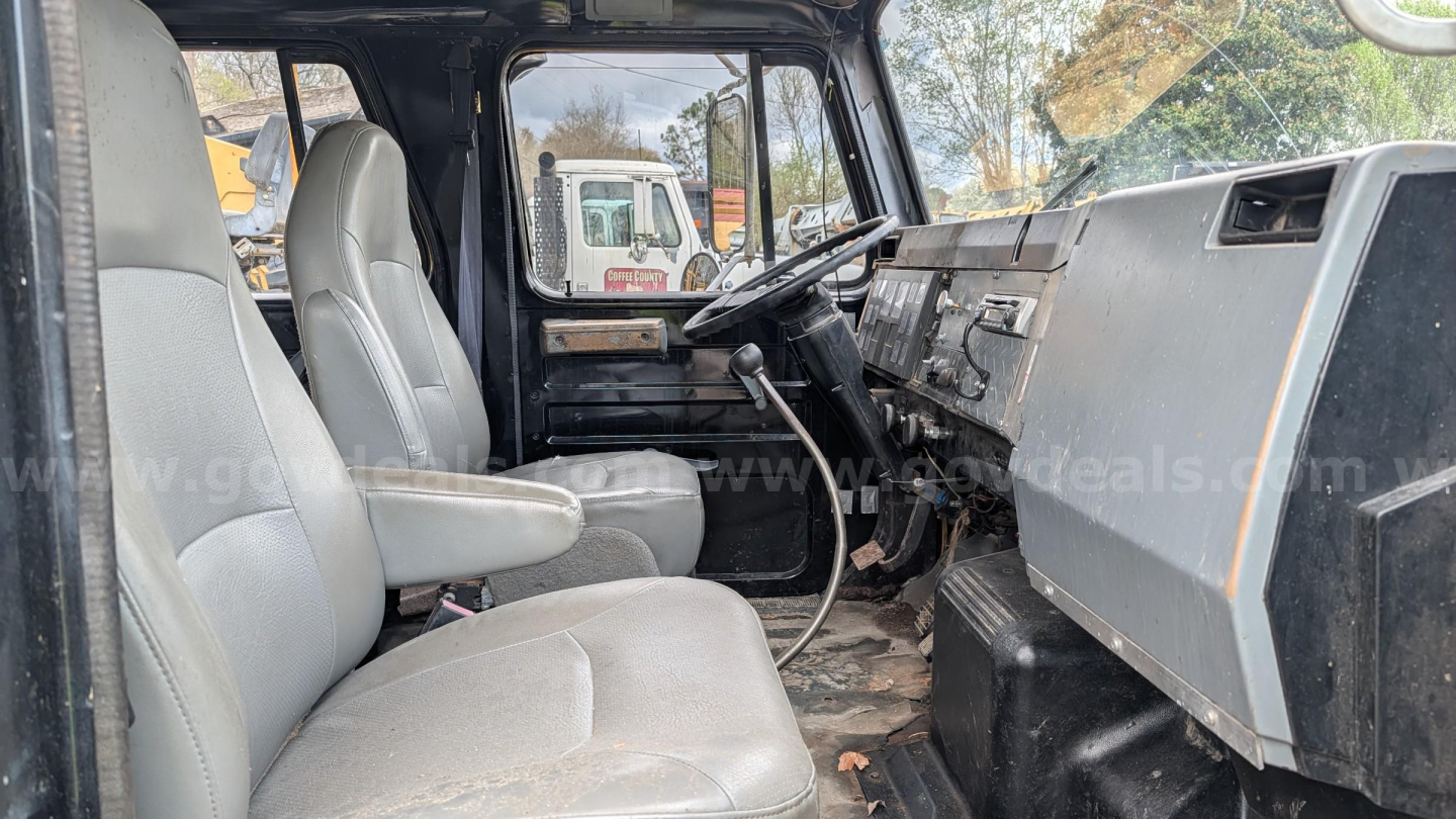 Truck interior of a 1990 International 4700 dump truck showing two front seats, steering wheel, dashboard and center console.