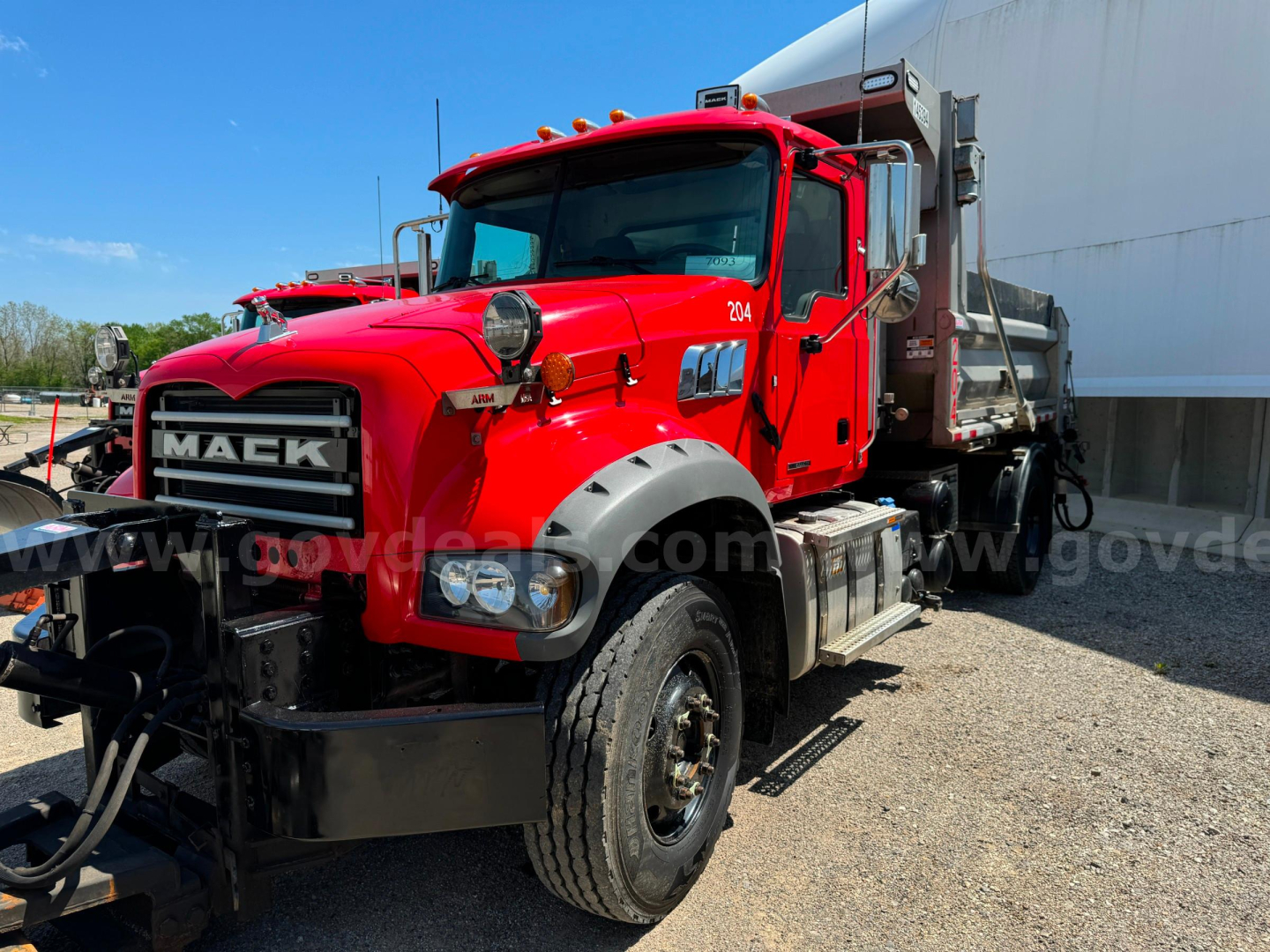 Red 2019 Mack Granite plow truck in-service showing front grille with MACK letters, dual round headlights, side mirrors, and wheel, with plow equipment and dumping bed visible.