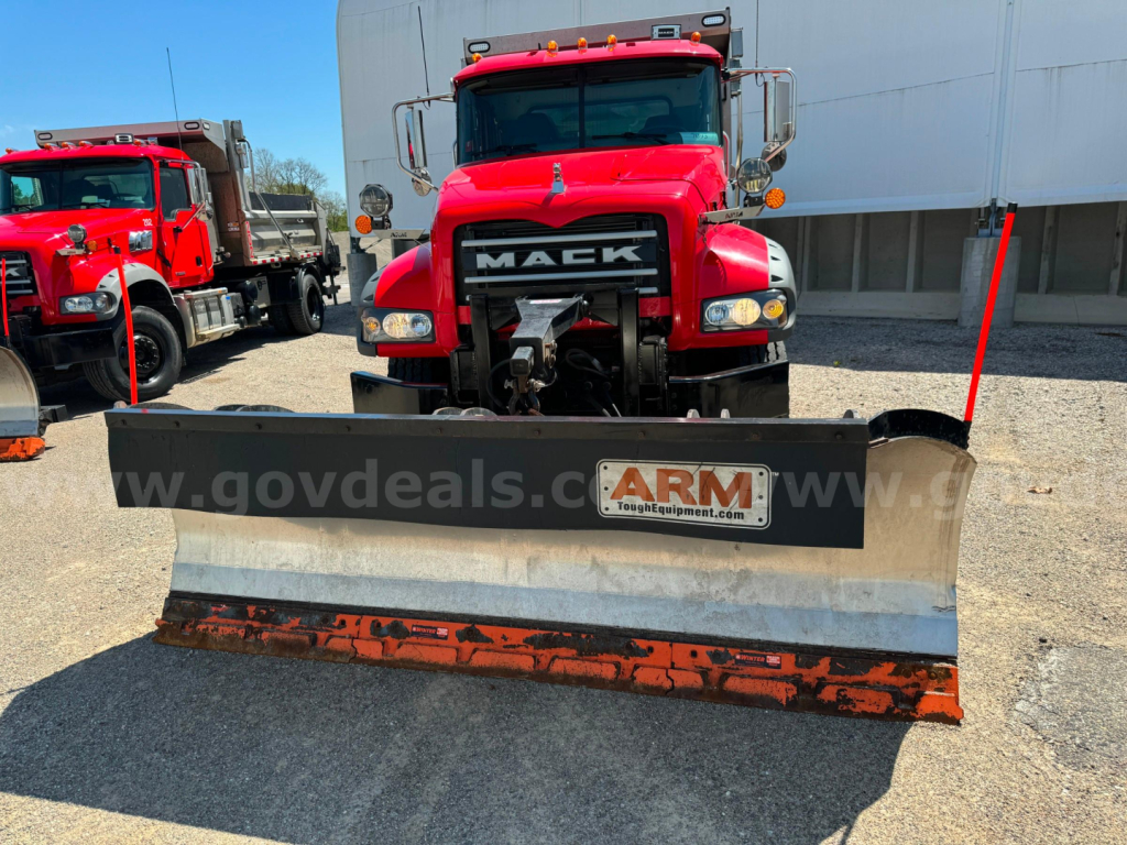 Mack Granite front view with snow plow blade attached, red truck, headlights, grille with MACK logo, plow mounting, road grime on plow edge