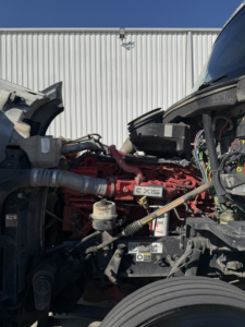 Kenworth truck engine bay with red engine block and various hoses and components; visible label reading 6 XIS? and wiring harnesses.
