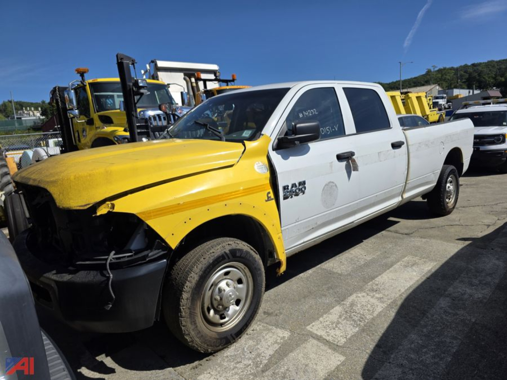 Front-left view of a white 2016 Ram 2500 pickup with a yellow front fender and hood damage, visible in a lot among other heavy equipment.