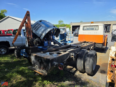 Chassis of a 1984 International 1700 showing a blue engine hoist and exposed drivetrain, with rear dual tires and a burnt black frame.