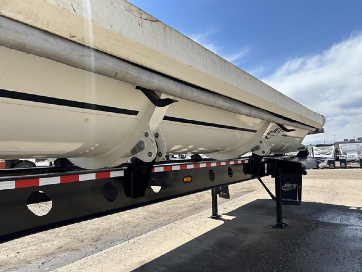 Trailer side dump with Jet Air Ride system, underside view showing support legs and frame, white body with black chassis, flatbed edge and hydraulic mechanism visible.