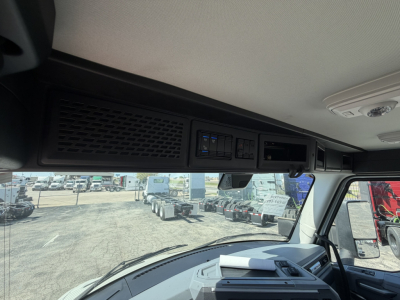 Cab interior overhead area showing controls and dash area with vents and a digital display, windshield and exterior lot visible.