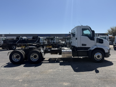 Side view of a white Mack AN64T conventional day cab chassis with empty frame and fuel tank, showing wheel rims and cab design.