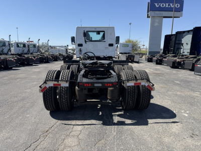 Rear view of a white Mack AN64T truck chassis in a dealership lot showing dual rear axles, fifth wheel, and surrounding trucks.