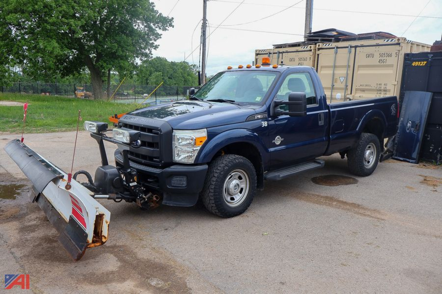 Ford F-350 Super Duty pickup with snow plow attached in a parking lot, navy blue crew cab long bed, front bumper winch mount.