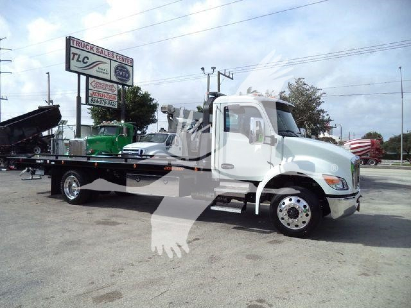 Kenworth T280 rollback truck side view showing flatbed and wheel details with dealership signage in background.