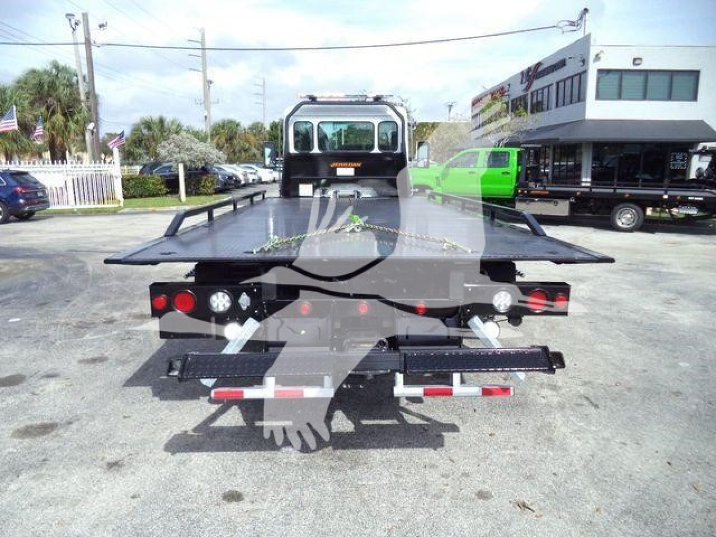 Rear view of a 2025 Kenworth T280 rollback truck with a long flatbed; taillights, hydraulic controls, and towing hitch visible.