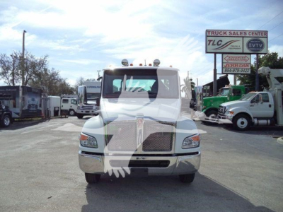 Truck front view of a white Kenworth T-series rollback truck with a large chrome grille and rectangular headlights.