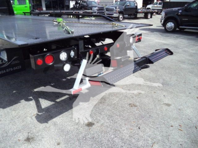 Kenworth T280 rollback tow truck rear with hydraulic bed and ramp, black steel chassis, red taillights, multiple gauges visible on control panel.