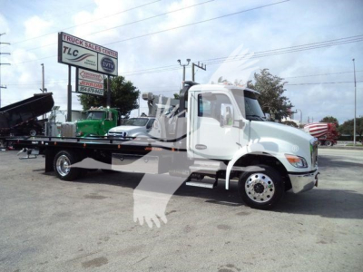 Kenworth T280 rollback truck side view showing flatbed and wheel details with dealership signage in background.