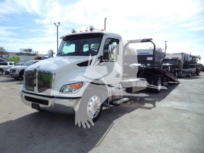 Kenworth T280 rollback tow truck in a lot, front grille and cab visible with a hydraulic bed trailer attached; no legible technical labels visible on the image.