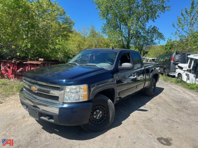 Chevrolet Silverado 1500 extended cab pickup truck in blue, front three-quarter view, with 4x4 badge visible, parked on a dirt lot with trees in background.