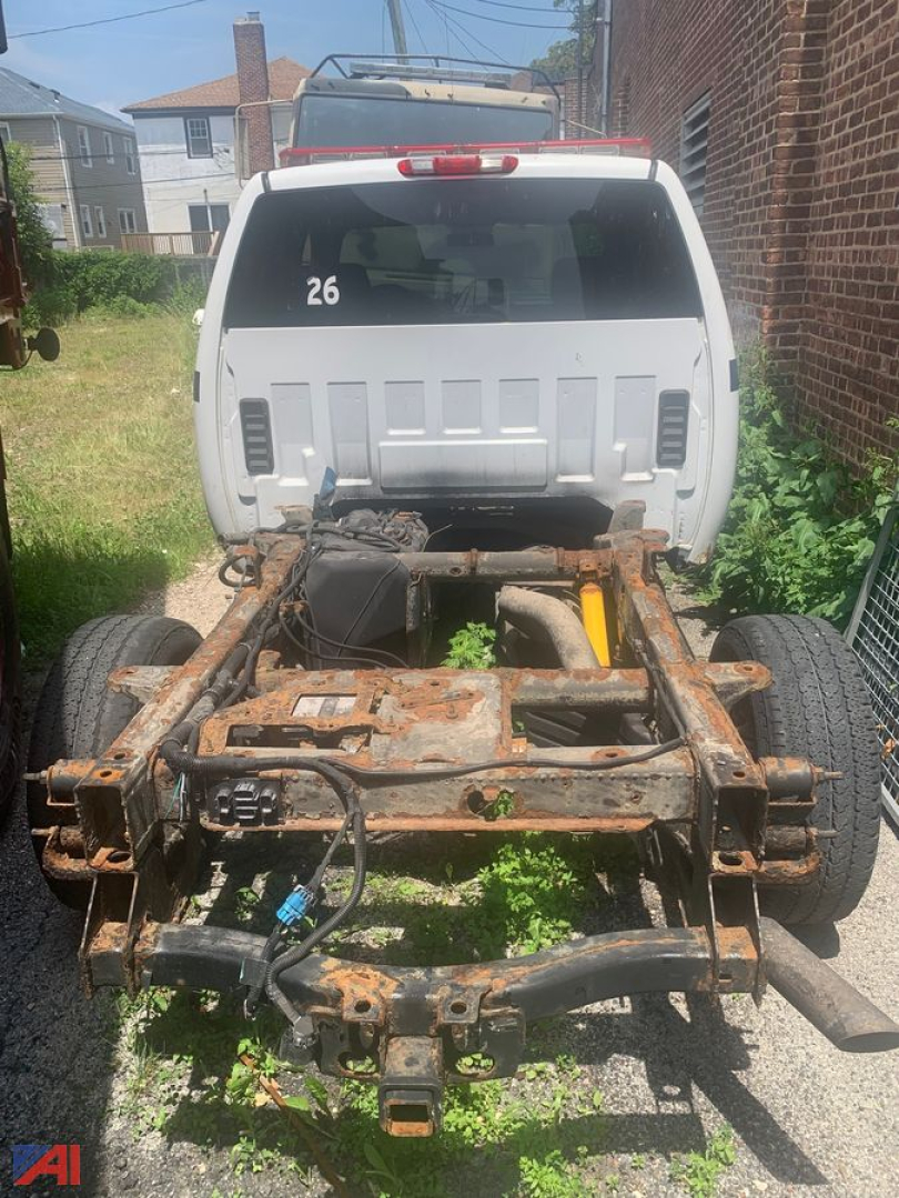 Rear view of a white Chevrolet Silverado 2500HD chassis with exposed rusty frame and drivetrain, 4x4 pickup, number 26 on rear window.