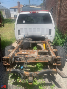 Rear view of a white Chevrolet Silverado 2500HD chassis with exposed rusty frame and drivetrain, 4x4 pickup, number 26 on rear window.