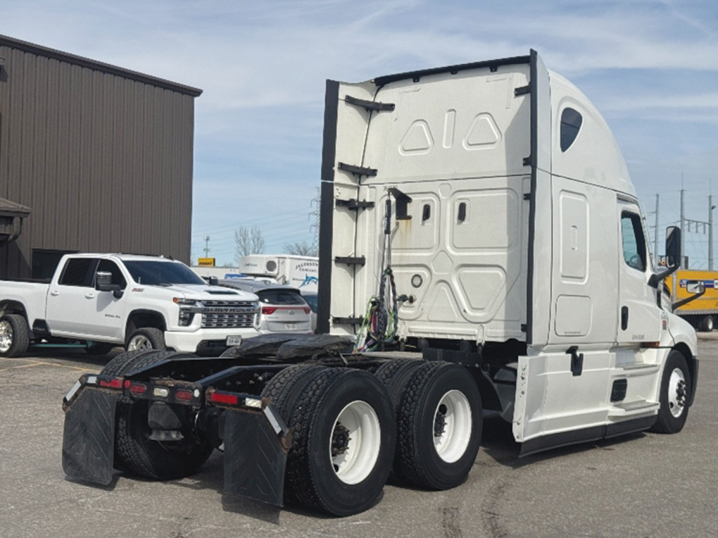 Truck cab rear view with sleeper, showing Freightliner Cascadia 126 model details not visible on image, but the vehicle is a white semi-truck with triple rear axles.