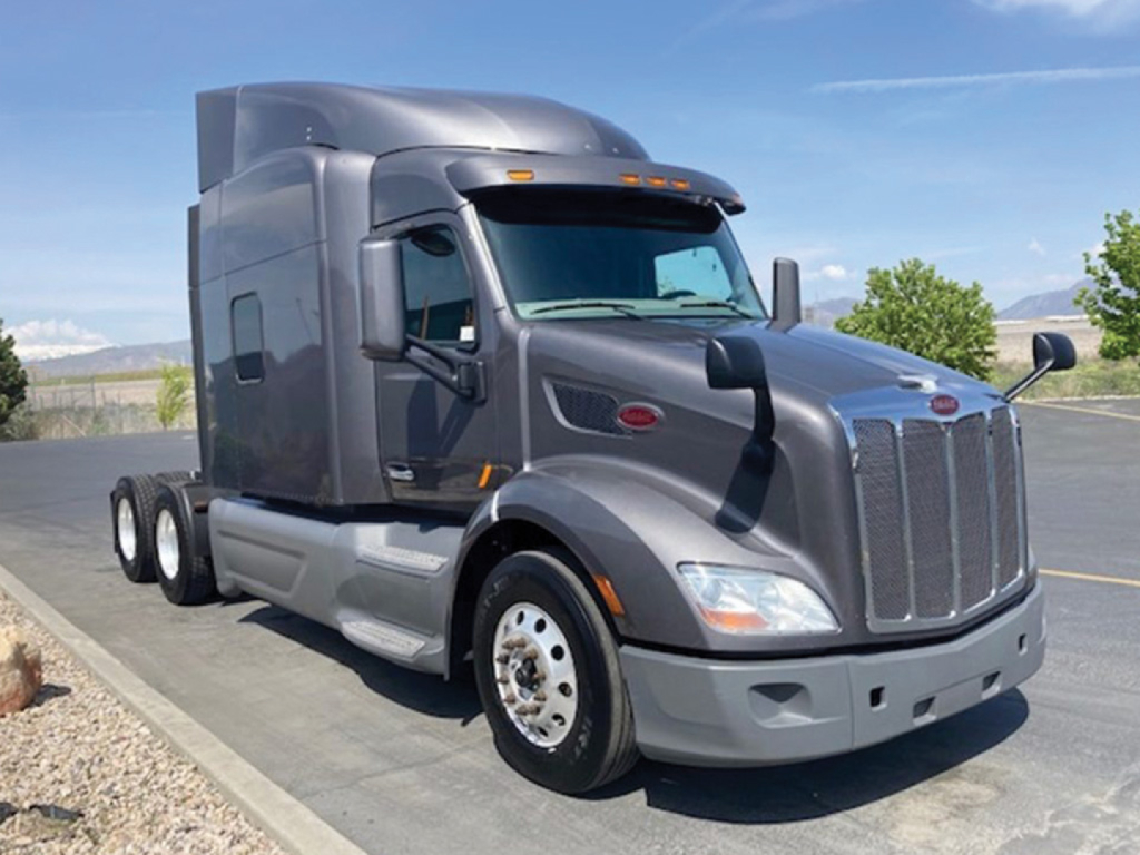 Peterbilt 579 UltraCab tractor viewed from front-left side. Features include large grille, chrome bumper, dual fuel tanks, grey paint, and Peterbilt emblem on hood.