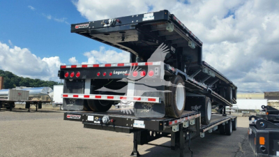 Manac drop deck trailer viewed from rear-right, with black frame, red/white reflective tape, and multiple axles; rear bumper shows Legend Trucks branding and taillights.