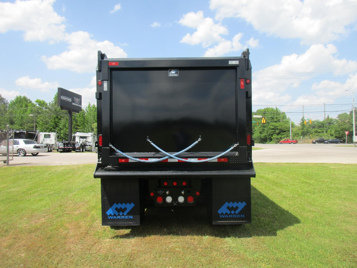 Dump truck bed of a new Western Star 49X back view showing a black dump body with blue Warnert logos on the mud flaps and tailgate latches, clear sky.
