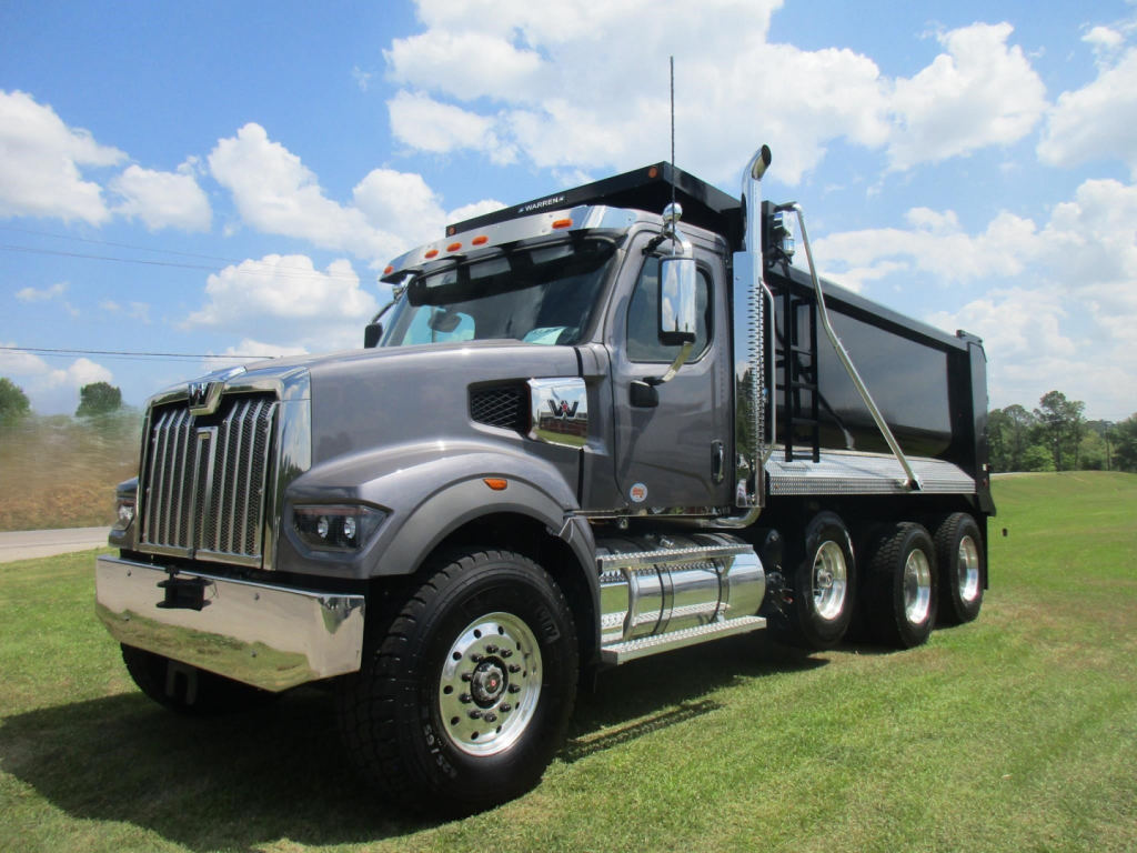 Truck image: 2026 Western Star 49X dump truck with gray cab, black grille, chrome bumper, and dump bed on a grassy field.