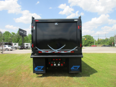 Dump truck bed of a new Western Star 49X back view showing a black dump body with blue Warnert logos on the mud flaps and tailgate latches, clear sky.
