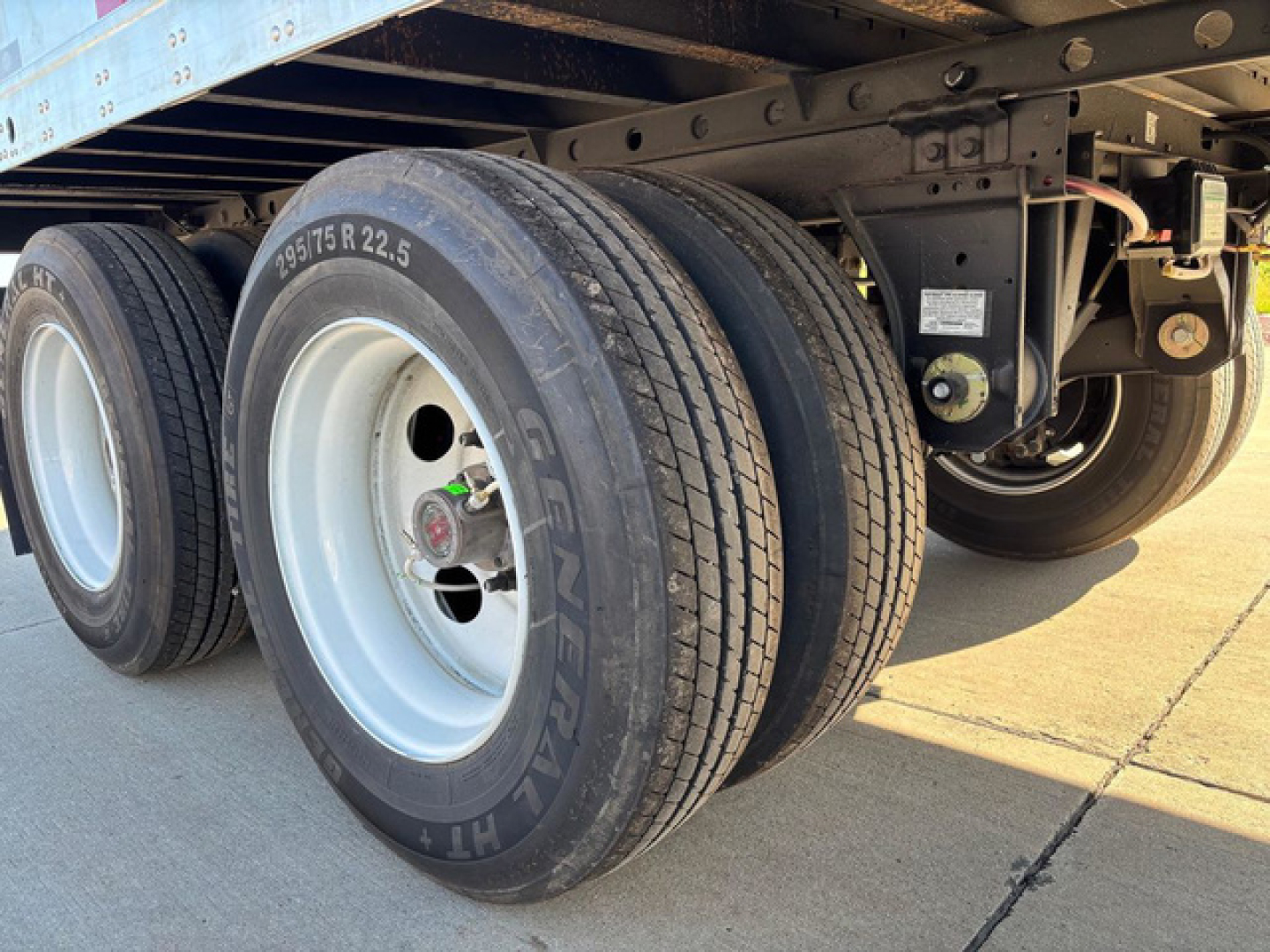 Trailer axle with dual rear wheels and tire treads, part of a Utility Dx trailer. Visible text on tire reads '195/75R22.5' and 'GENTRAI' around the rim; underside frame and suspension hardware visible.
