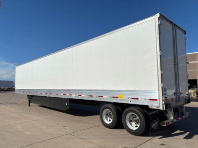 Large white utility trailer with double rear doors and tandem axles, side marker lights, in a parking lot.