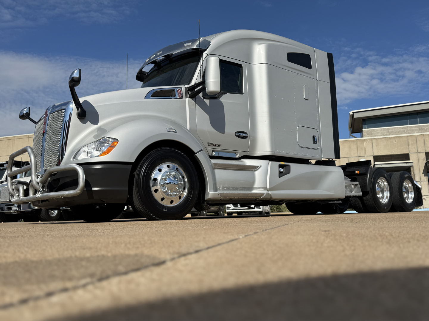 Kenworth T680 conventional sleeper tractor in silver, side view showing cab with sleeper, front bumper and chrome wheels.