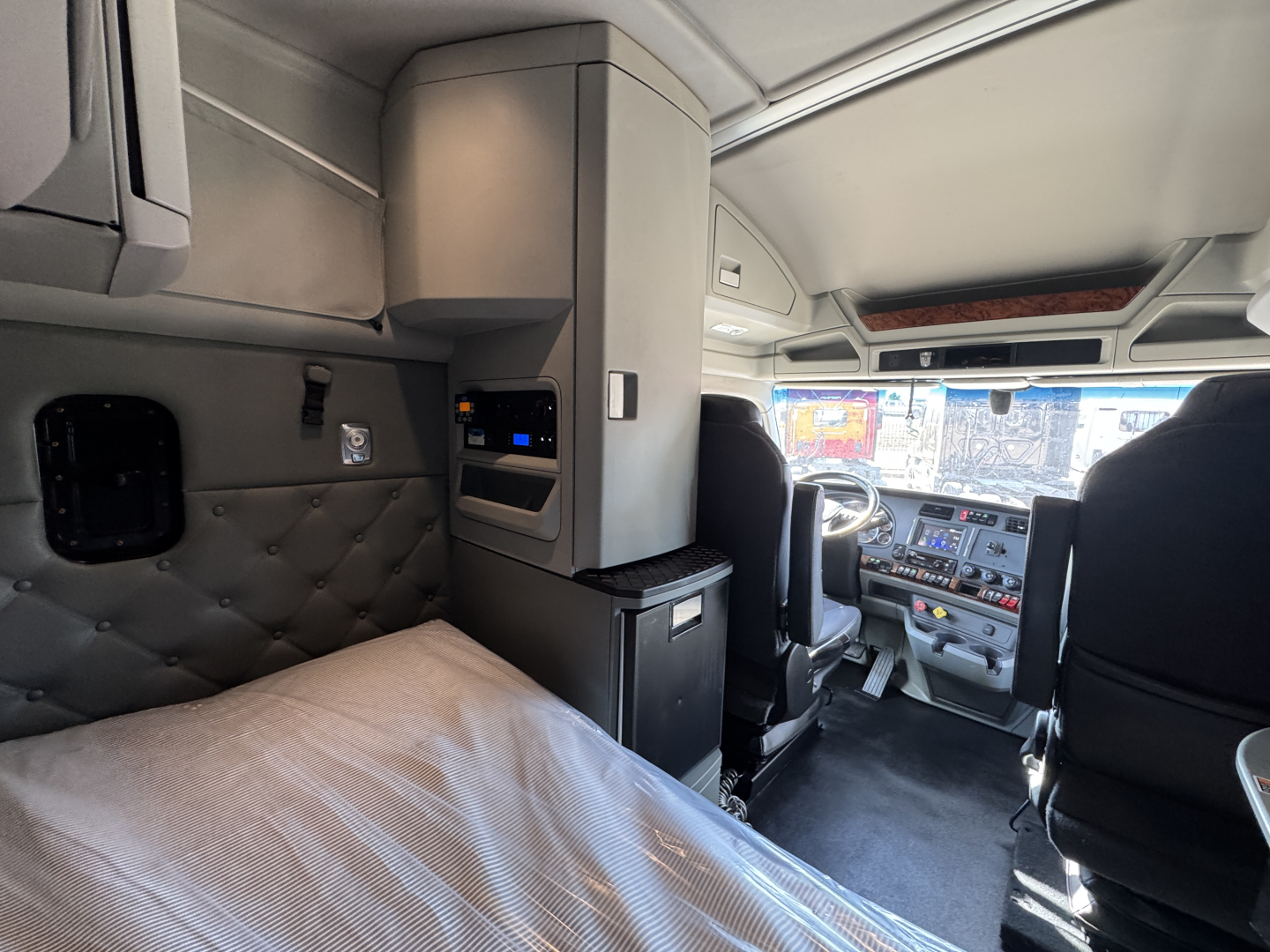Kenworth T680 sleeper cab interior with side bunk and driver seat, dashboard visible, overhead cabinets.