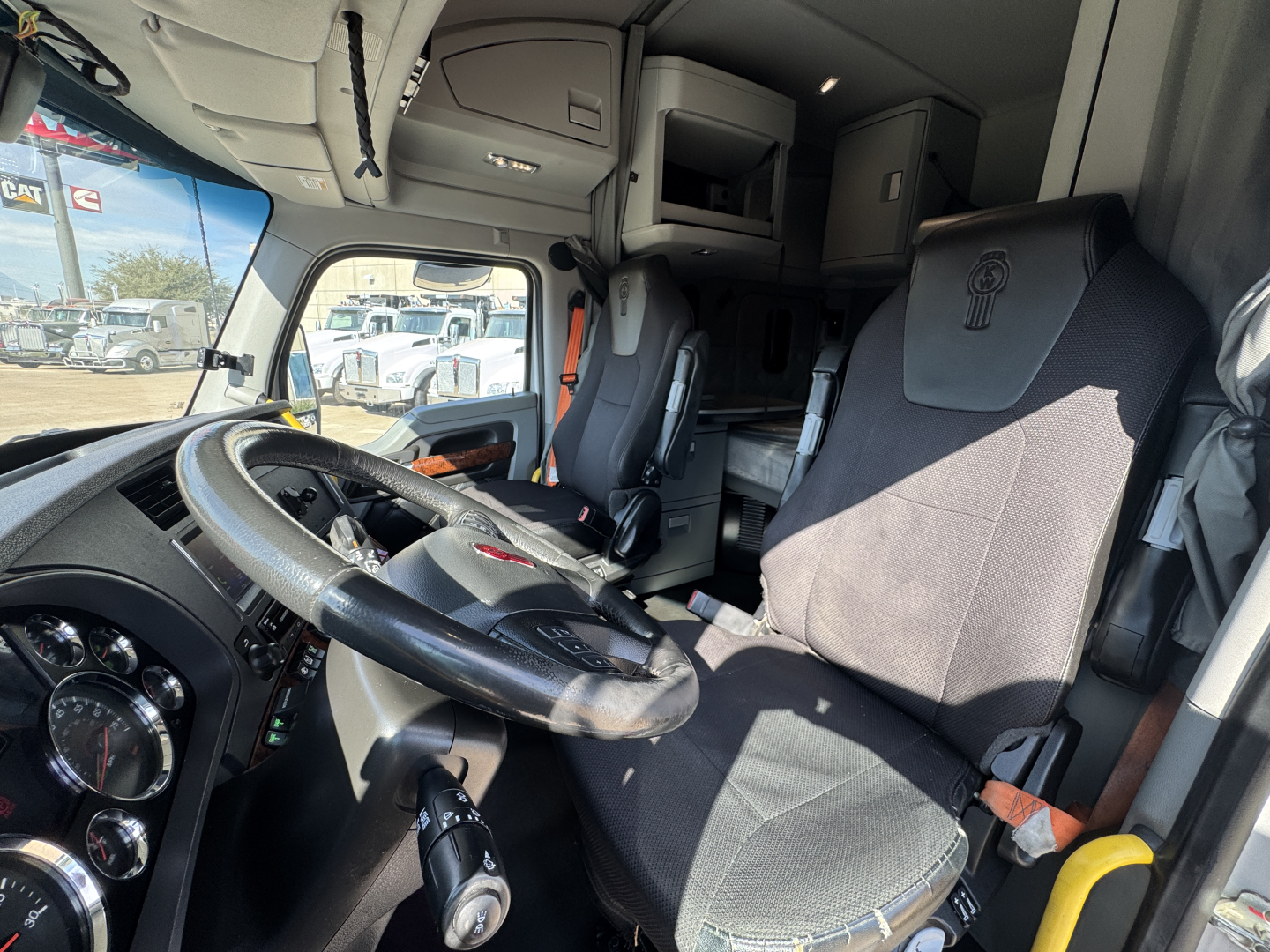 Kenworth T680 truck interior showing steering wheel, dashboard, and driver seat with sleeper cab area in view.