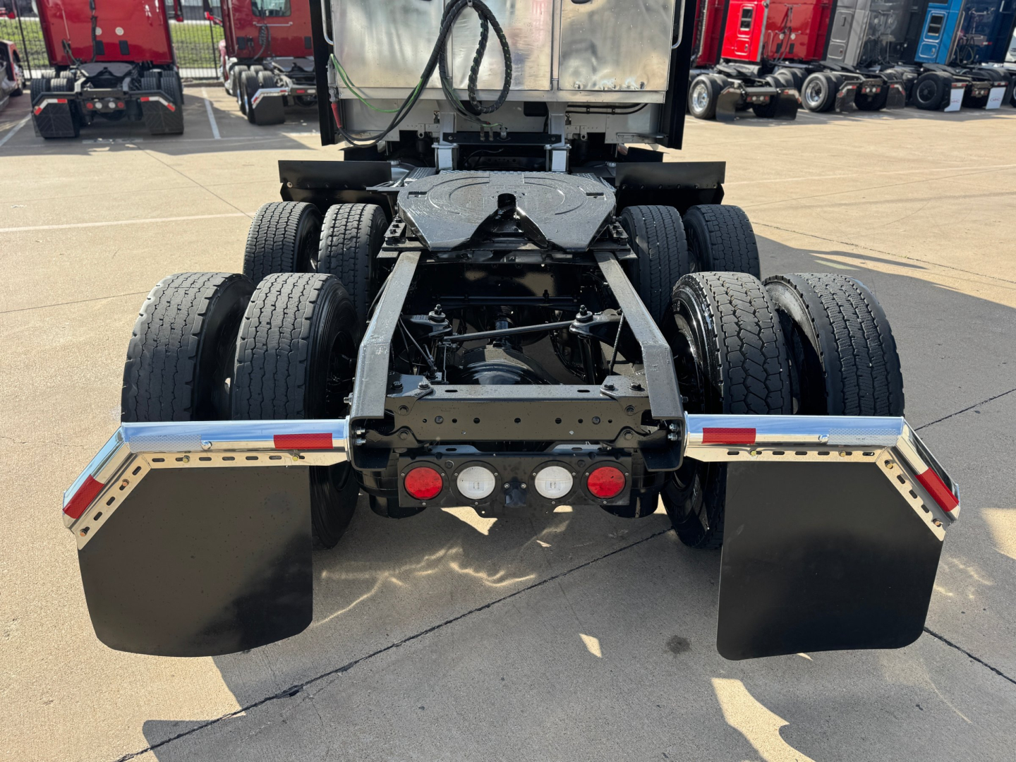 Kenworth T680 rear view showing dual rear axles, fifth wheel area, and mud flaps. Visible are the chassis frame, rear bumper with lights, and mounting brackets.