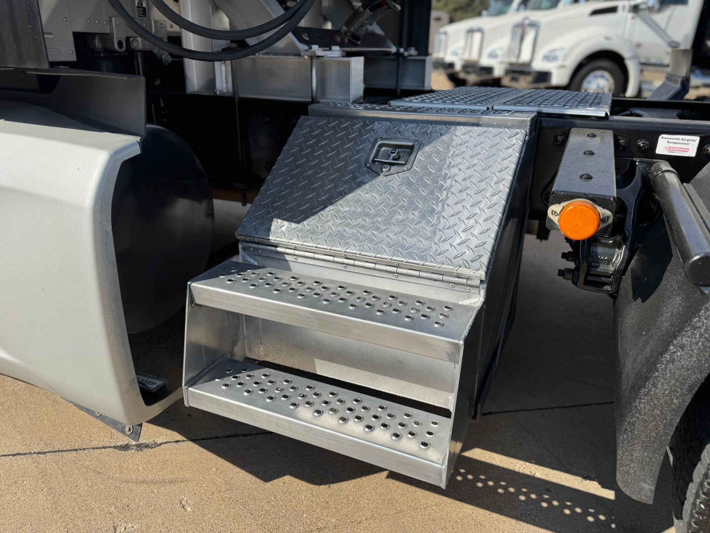 Kenworth T680 side step access platform with diamond plate metal steps and orange turn signal/marker light nearby.