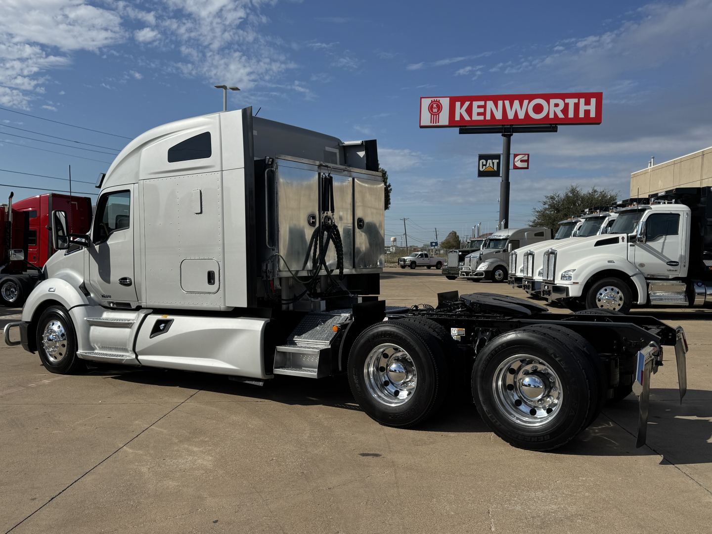 Kenworth T680 tractor in a used trucks lot, side view showing sleeper cab and rear dual axles with chrome wheels.