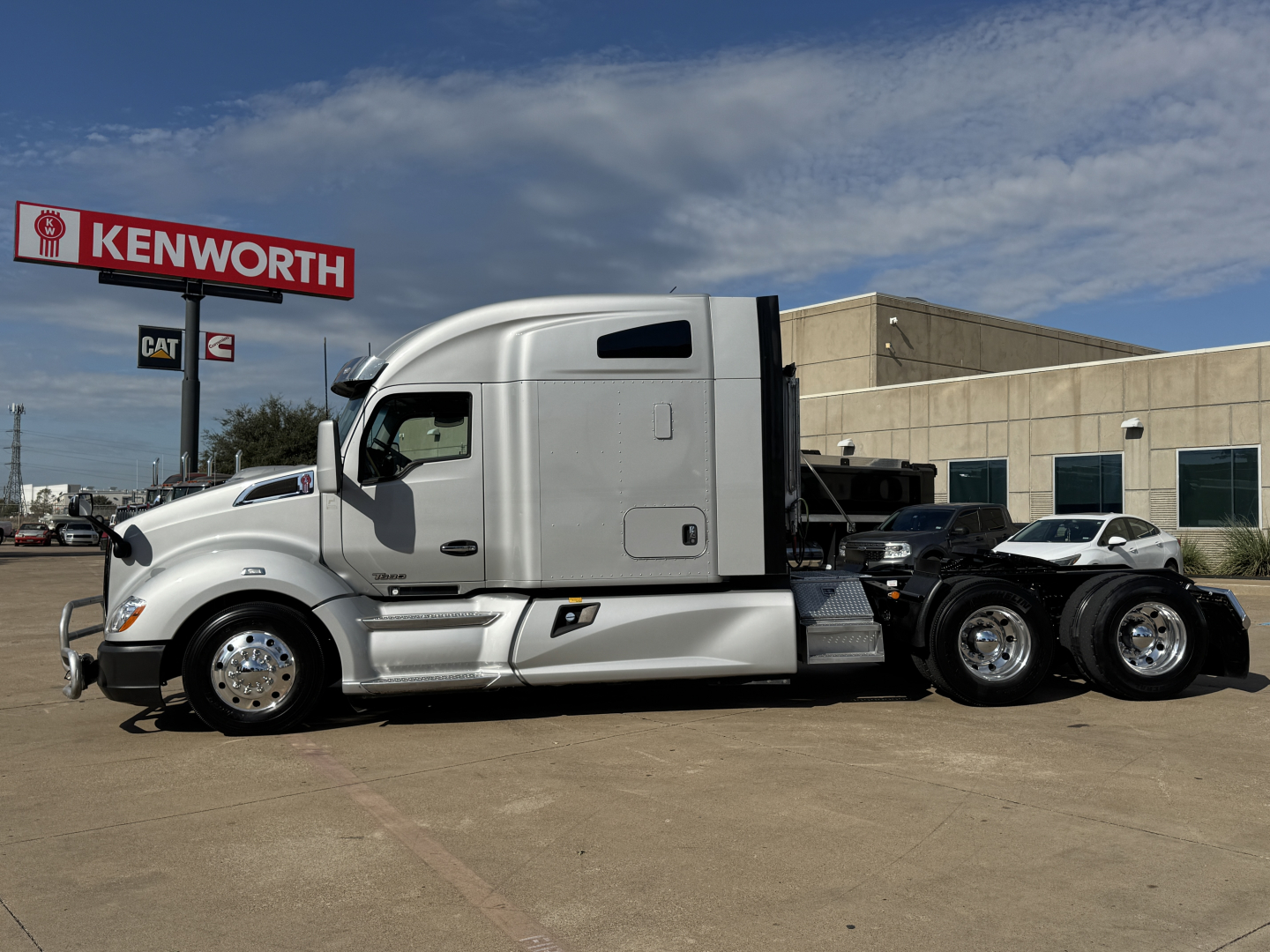 Kenworth T680 truck in a dealership lot with Kenworth sign in background.