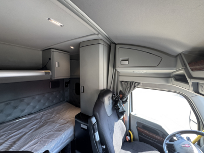 Kenworth T680 cab interior showing sleeper berth with quilted padding, overhead storage, and driver seat; dashboard and windshield visible.