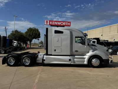 Kenworth T680 conventional sleeper tractor with silver exterior, side view showing cab, dual rear axles, Kenworth sign in background.