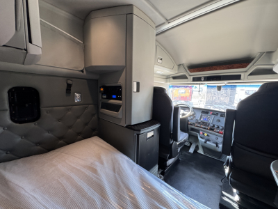 Kenworth T680 sleeper cab interior with side bunk and driver seat, dashboard visible, overhead cabinets.