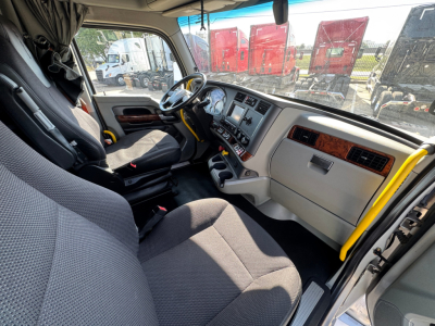 Kenworth T680 interior cab view showing steering wheel and dashboard with fabric seats and beige panels.