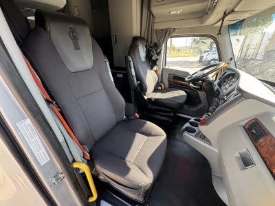 Kenworth T680 interior cab view showing front seats and steering wheel with driver seat belt visible.