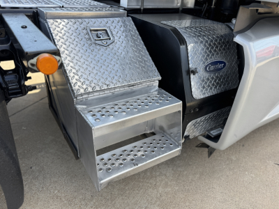 Kenworth T680 side step area with diamond plate toolbox and perforated metal step showing Carrier badge and chassis details.