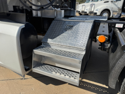 Kenworth T680 side step access platform with diamond plate metal steps and orange turn signal/marker light nearby.