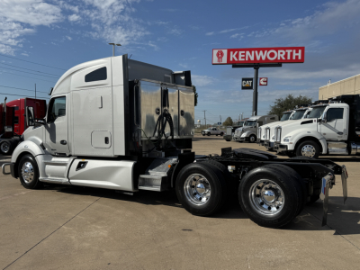 Kenworth T680 tractor in a used trucks lot, side view showing sleeper cab and rear dual axles with chrome wheels.