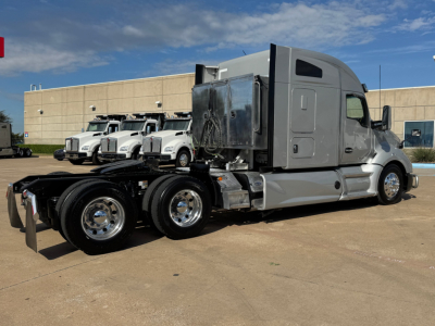 Kenworth T680 tractor cab and chassis in a parking lot, side view showing dual rear axles and fuel tanks, with a metallic gray cab and black chassis.