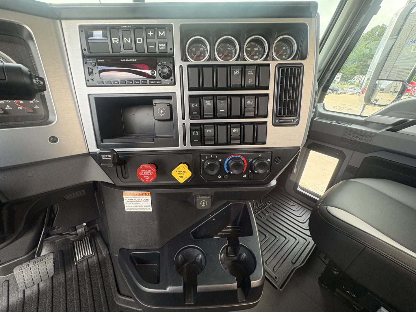 Dashboard of a new 2027 Mack PI64T truck showing gauge cluster, control switches, and gear selector with multiple push buttons and climate controls.
