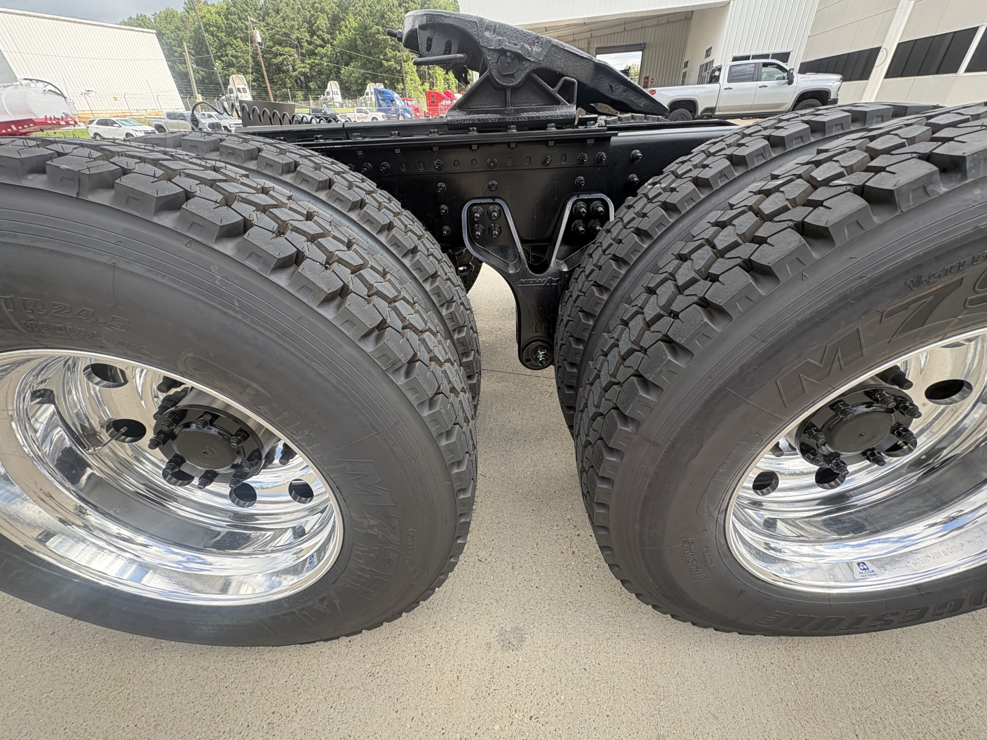 Mack PI64T dual rear axles with large off-road tires and polished chrome wheels, center view of chassis with fifth wheel and suspension components visible.