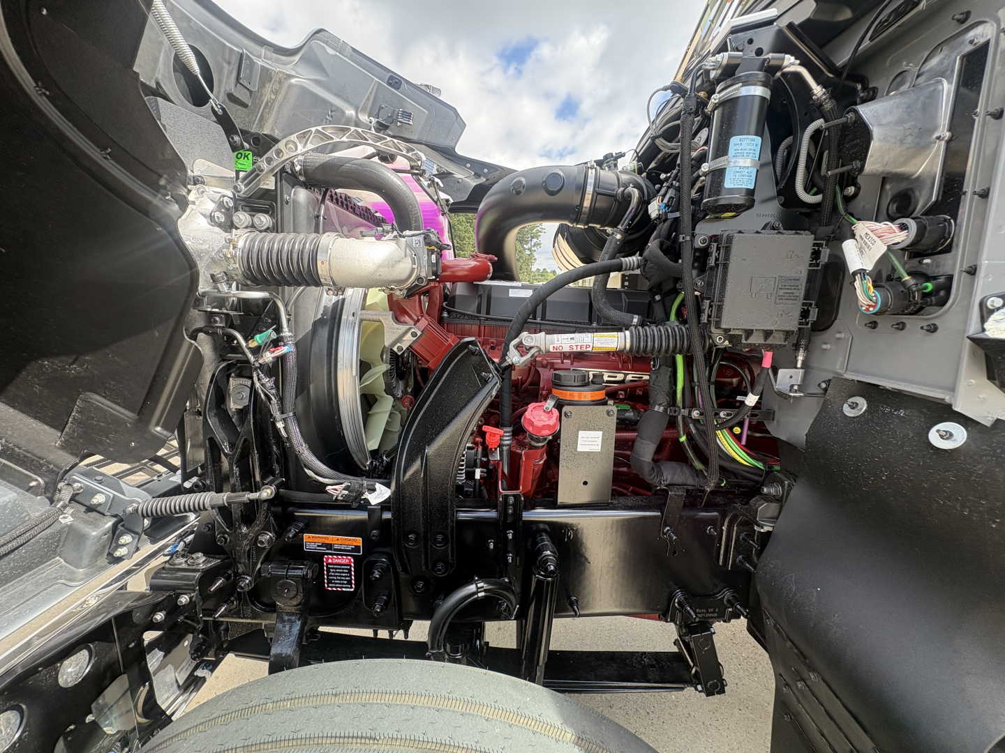 Mack PI64T engine bay showing coolant reservoir, air intake, hoses, wiring harness, and engine components as seen from under the cab.