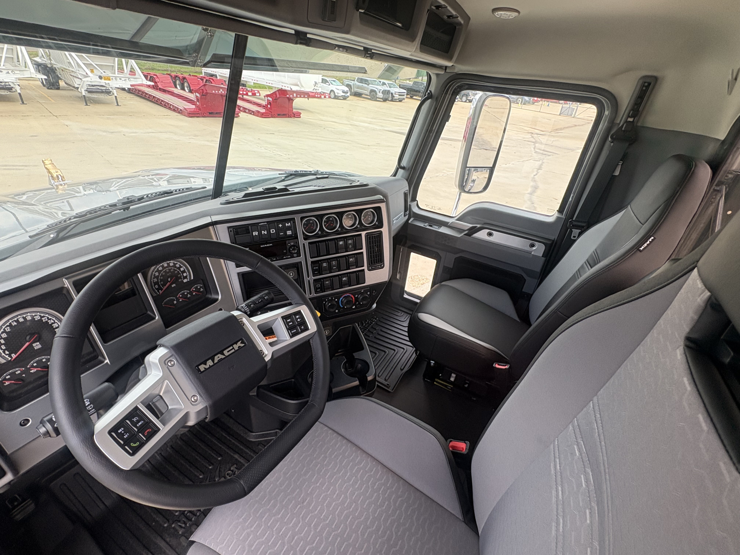 Interior of 2027 Mack PI64T truck cab showing steering wheel, dashboard with multiple gauges, center console, and driver seat.